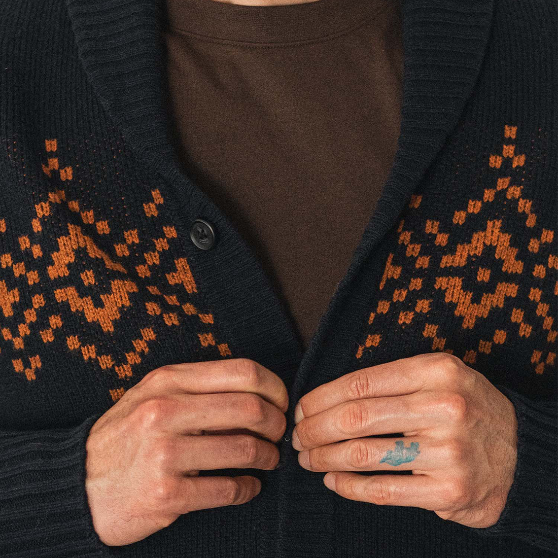 Close up of hands buttoning the Sprague shawl collar cardigan in Highland Dusk, showing the burnt orange knit pattern - The Simple Man