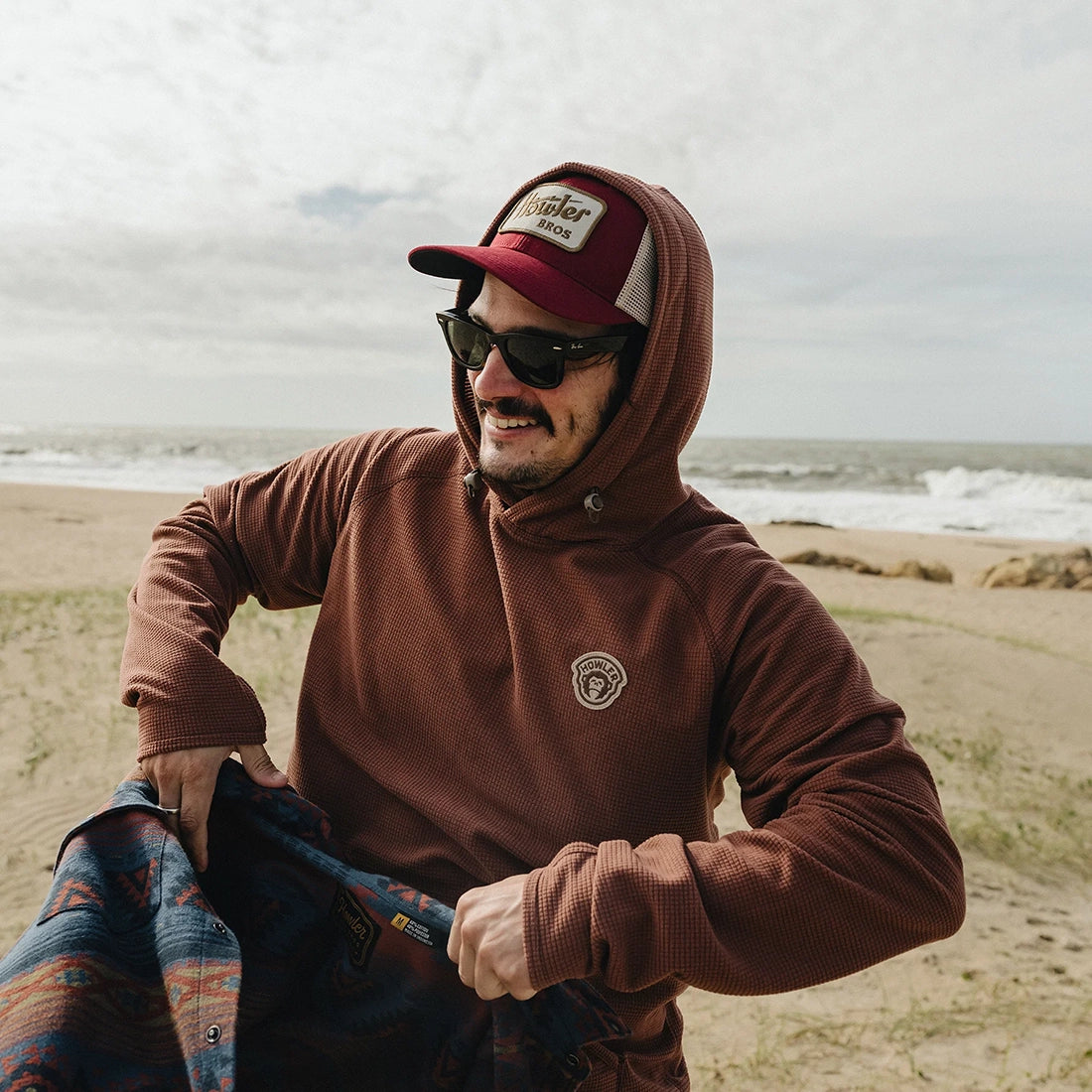 Man wearing the Howler Electric Standard Hat in Burgundy at the beach, burgundy trucker cap with Howler Bros patch, lifestyle shot -- The Simple Man