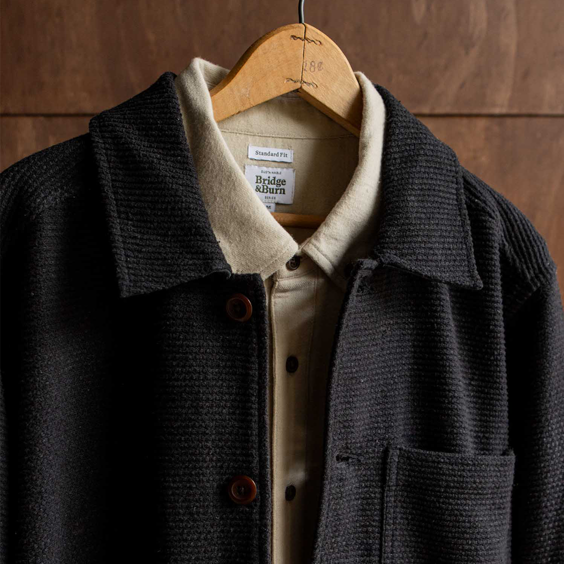 Close-up of Studio Chore Coat in Washed Black on hanger showing collar, chest pocket, and Bridge and Burn Sustainable Series label - The Simple Man
