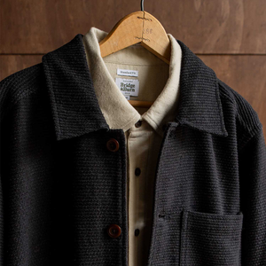 Close-up of Studio Chore Coat in Washed Black on hanger showing collar, chest pocket, and Bridge and Burn Sustainable Series label - The Simple Man
