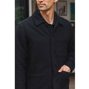 Man wearing Studio Chore Coat in Washed Black holding coffee mug in doorway, side profile styled with tan pants - The Simple Man