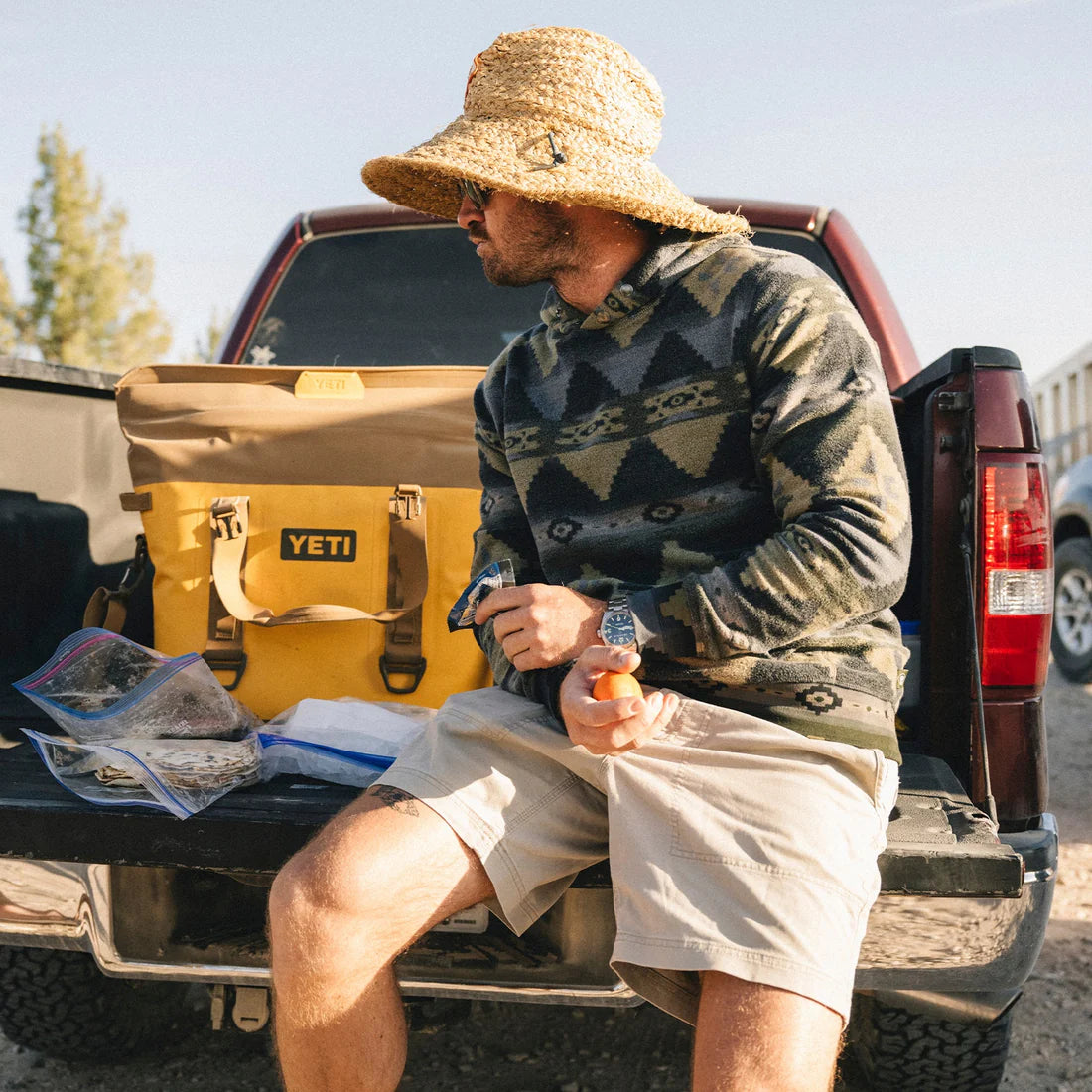 Man wearing Tajima Hoodie with Mitla pattern, sitting on truck tailgate with yellow Yeti cooler – rugged men's fleece hoodie at The Simple Man Omaha