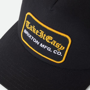 Brixton Take It Easy Washed Black trucker hat patch close-up — gold merrowed edge embroidered patch with old English script on black