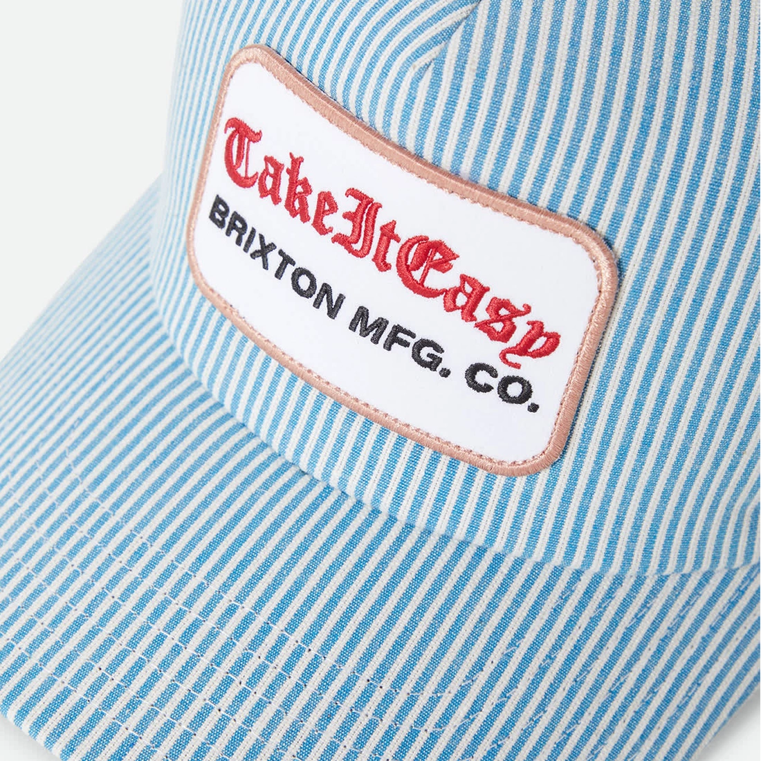 Brixton Take It Easy trucker hat patch close-up — merrowed edge embroidered patch with red old English script on blue white stripe