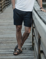 Man wearing The Normal Brand Storm Summer Short on wooden boardwalk with sandals – 7 inch stretch cotton short warm weather men's style
