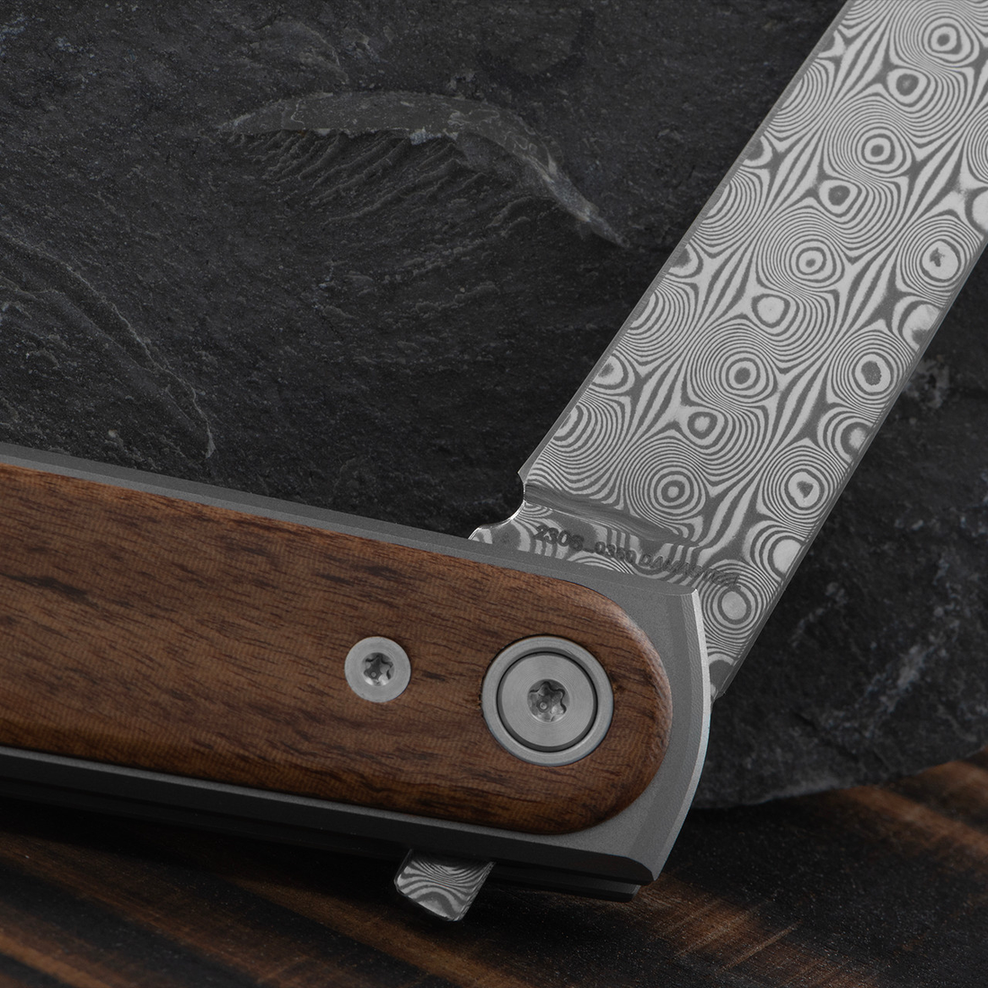 Close-up of the Duval's Damasteel blade pattern beside the rosewood scale and pivot