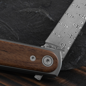 Close-up of the Duval's Damasteel blade pattern beside the rosewood scale and pivot
