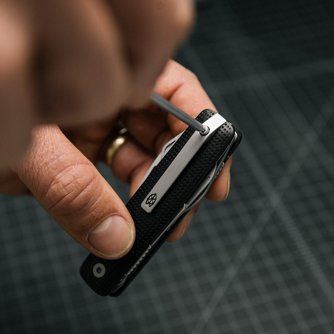 Hand holding the Helton while a small hex key turns the pocket clip screw