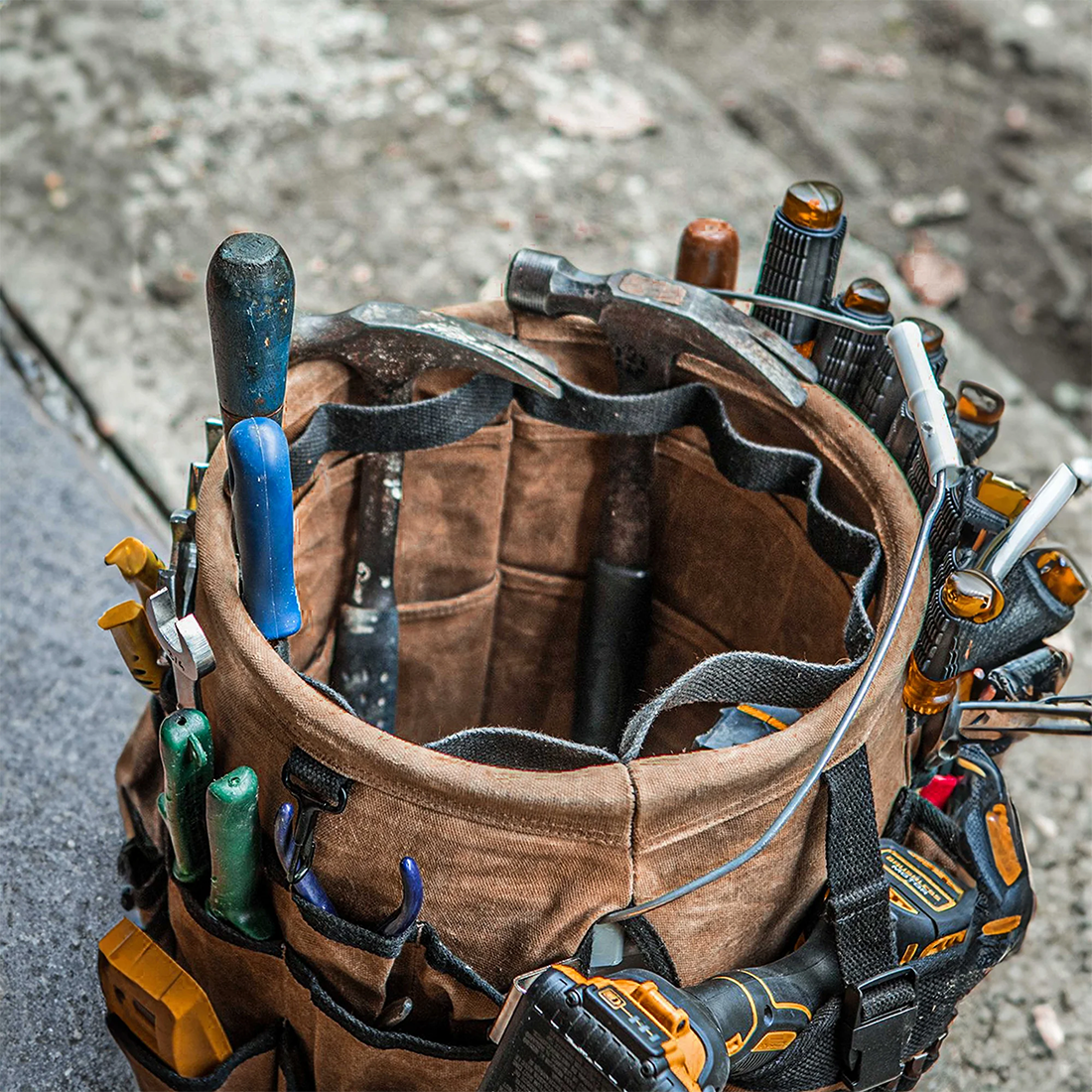 Readywares Waxed Canvas Tool Bucket Organizer, overhead view loaded with hammer, pliers, and drill on concrete
