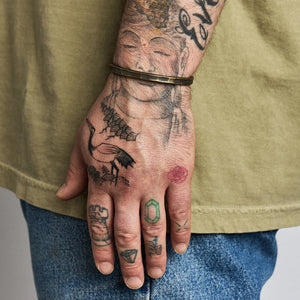 Model wearing Studebaker Metals brass Trench Cuff in Work Patina, shown on wrist with visible hand tattoos.