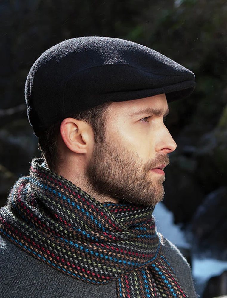 Man wearing a black wool Trinity Flat Cap outdoors, styled with a patterned winter scarf from The Simple Man