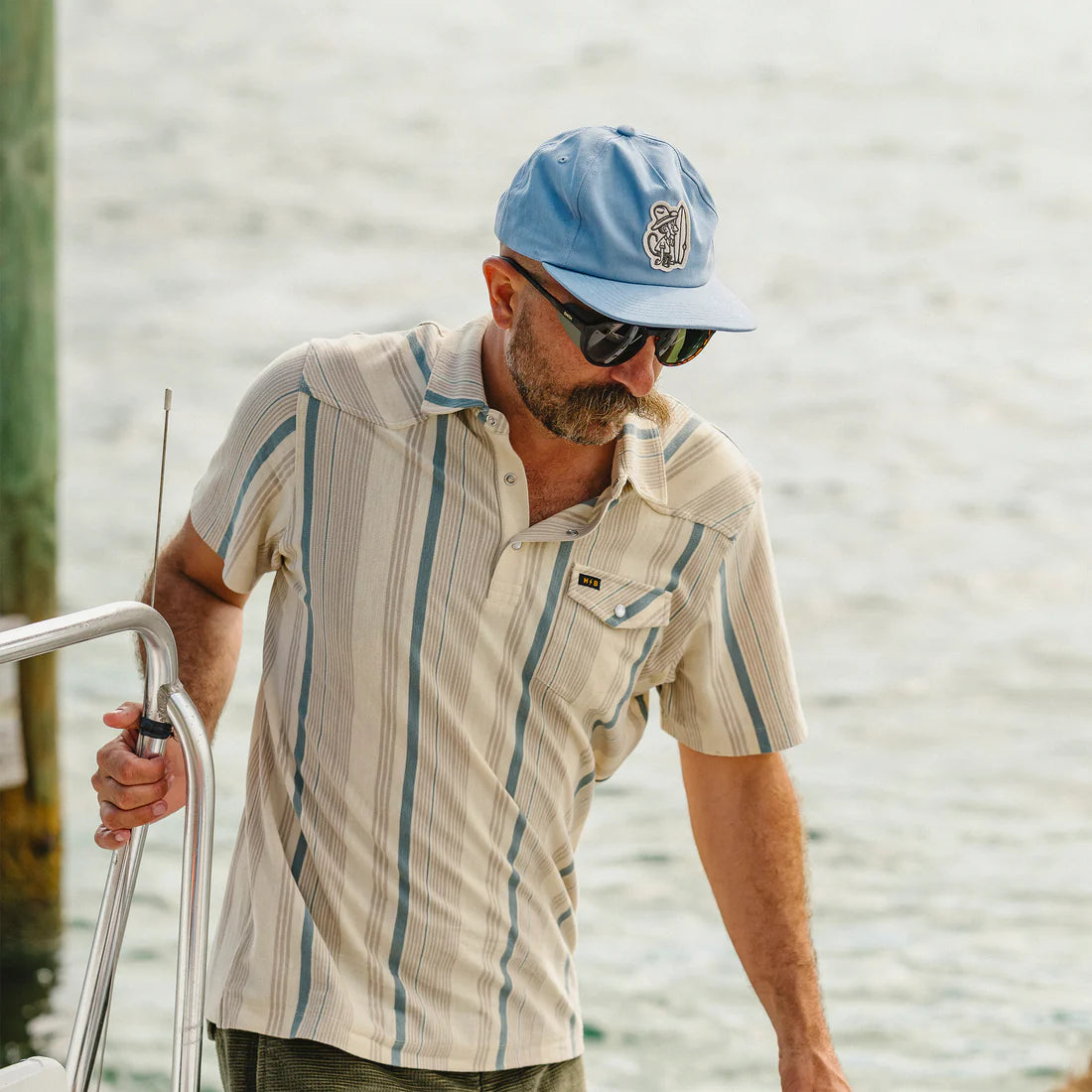 Man wearing Howler Brothers El Monito Surfs Snapback in Blue on boat dock – men's unstructured snapback hat with patch logo