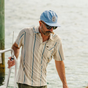 Man wearing Howler Brothers El Monito Surfs Snapback in Blue on boat dock – men's unstructured snapback hat with patch logo