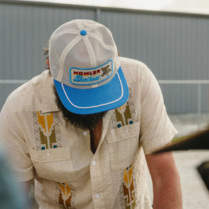 Man wearing Howler Brothers Osprey Prey Feedstore Snapback in Stone Blue – men's retro mesh trucker hat with embroidered patch and rope trim bill
