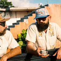 Two men wearing Howler Brothers Feedstore Snapback hats outdoors – men's vintage mesh trucker caps in stone blue and tan