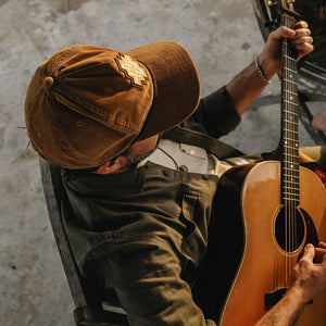 Man wearing the H Bolt Motif Unstructured Snapback Hat in Tan Corduroy while playing guitar, cream and yellow H Bolt diamond patch, lifestyle shot -- The Simple Man