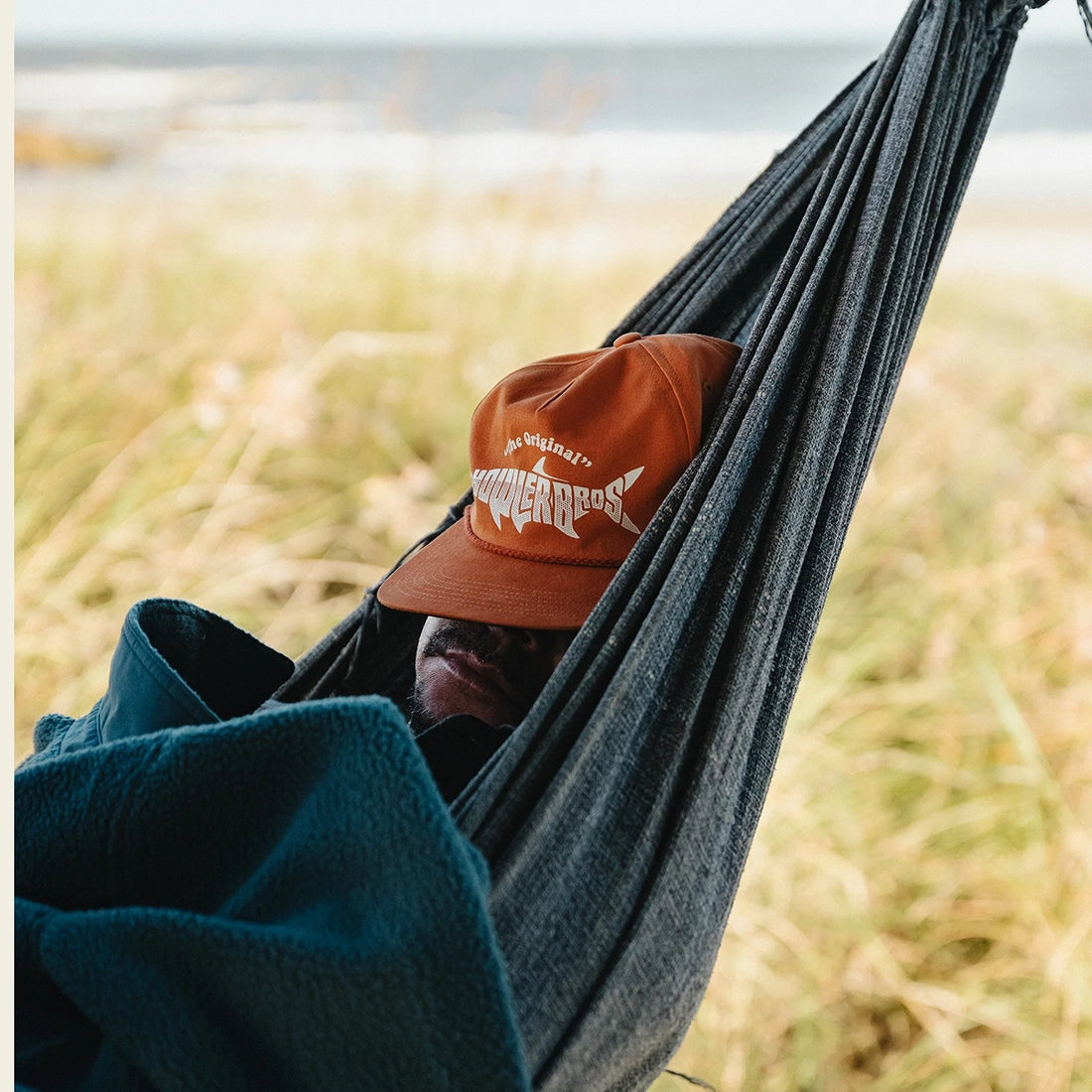Man wearing the Silver King Unstructured Snapback Hat in Toasted Orange while resting in a beach hammock, lifestyle shot -- The Simple Man
