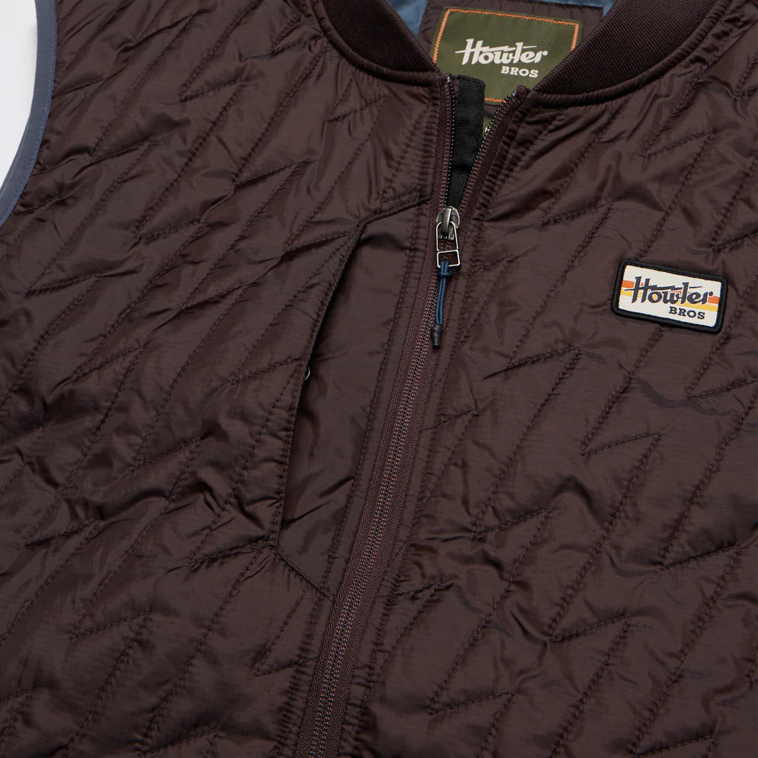 Close-up of Voltage Quilted Vest in Bark with lightning stitch detail and Howler Bros patch