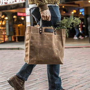 Model carrying Hardmill waxed canvas grocery tote in tan, full of groceries view