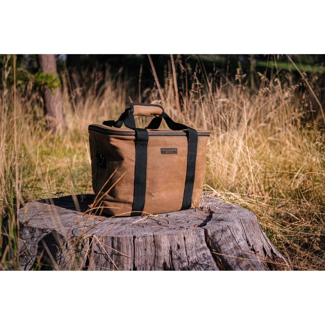 Waxed canvas cooler bag sitting on a tree stump in tall grass outdoors, The Simple Man