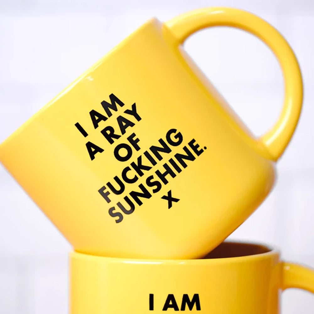 ellow coffee mug with "I'm a ray of Fucking Sunshine" in black screen print. 2 mugs stacked