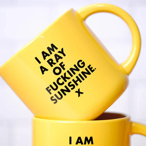 ellow coffee mug with "I'm a ray of Fucking Sunshine" in black screen print. 2 mugs stacked