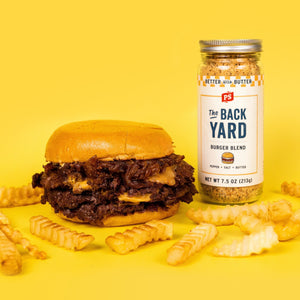 Double smashburger with melted cheese and caramelized onions next to The Backyard Burger Blend seasoning and crinkle-cut fries on a yellow background.