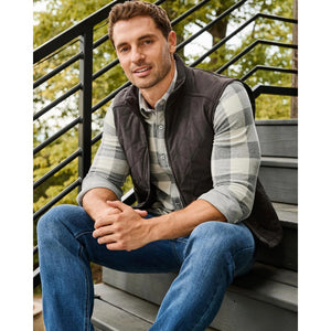 Charcoal quilted vest worn over a plaid shirt, man seated on outdoor steps