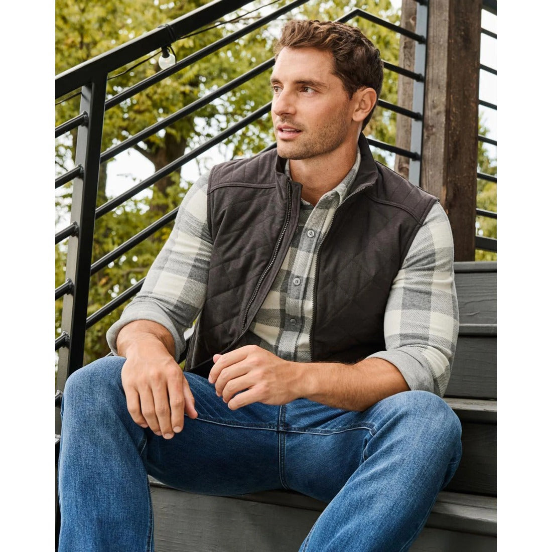 Charcoal diamond-quilted vest layered over a plaid button-down with jeans, outdoors