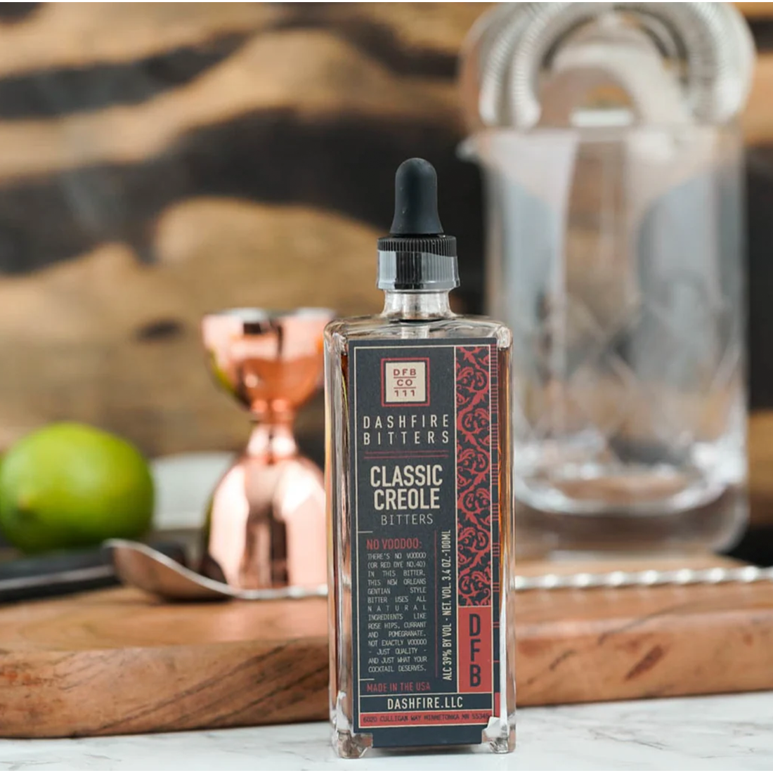 Bottle of Dashfire Bitters Classic Creole on a bar counter with cocktail tools in the background