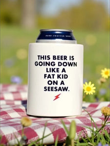 Fat Kid on a Seesaw beer koozie on a red-checked picnic blanket with wildflowers and a cold can of beer