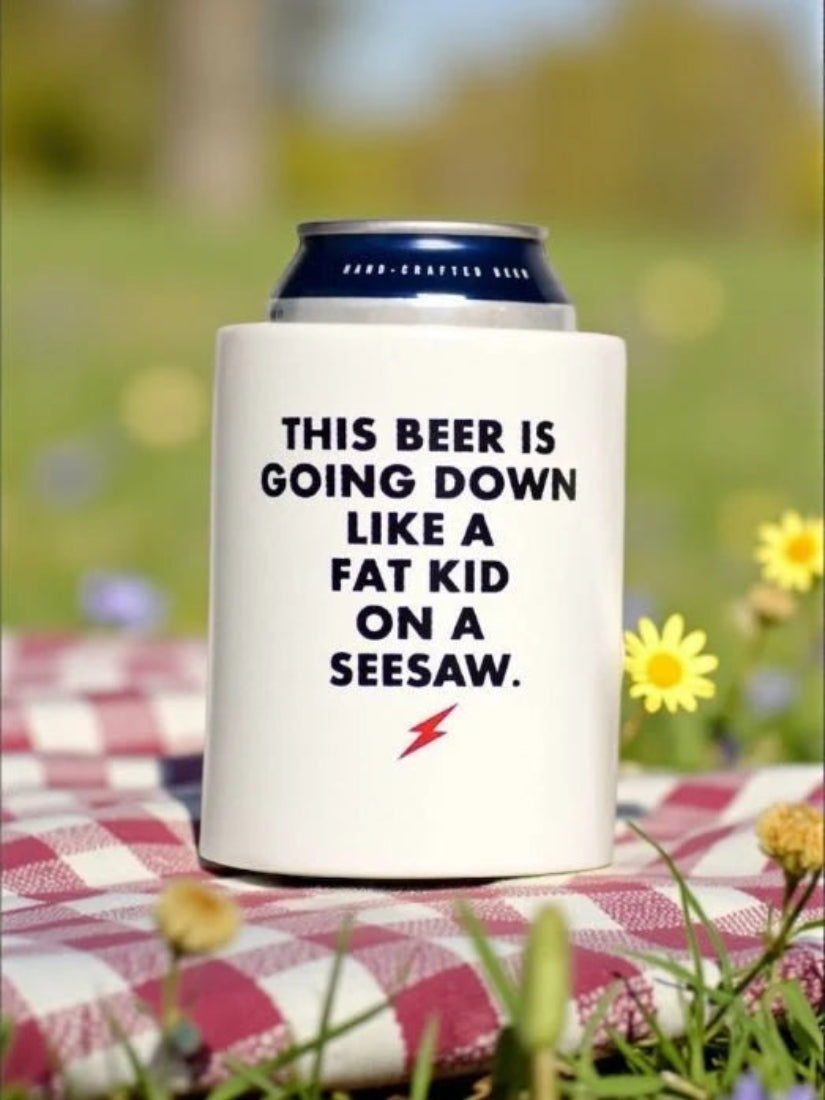 Fat Kid on a Seesaw beer koozie on a red-checked picnic blanket with wildflowers and a cold can of beer