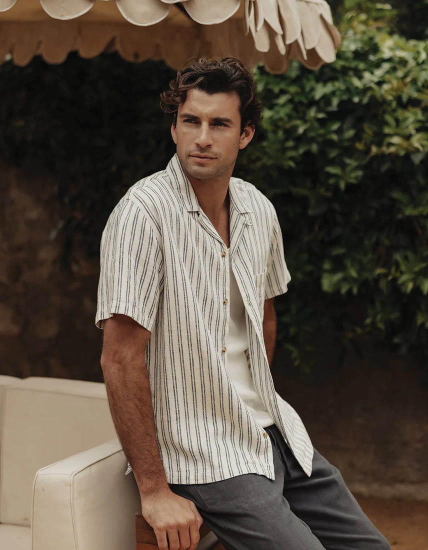 The Normal Brand Freshwater Resort Shirt Vintage Blue Stripe – model seated outdoors in men's relaxed fit linen rayon camp collar shirt