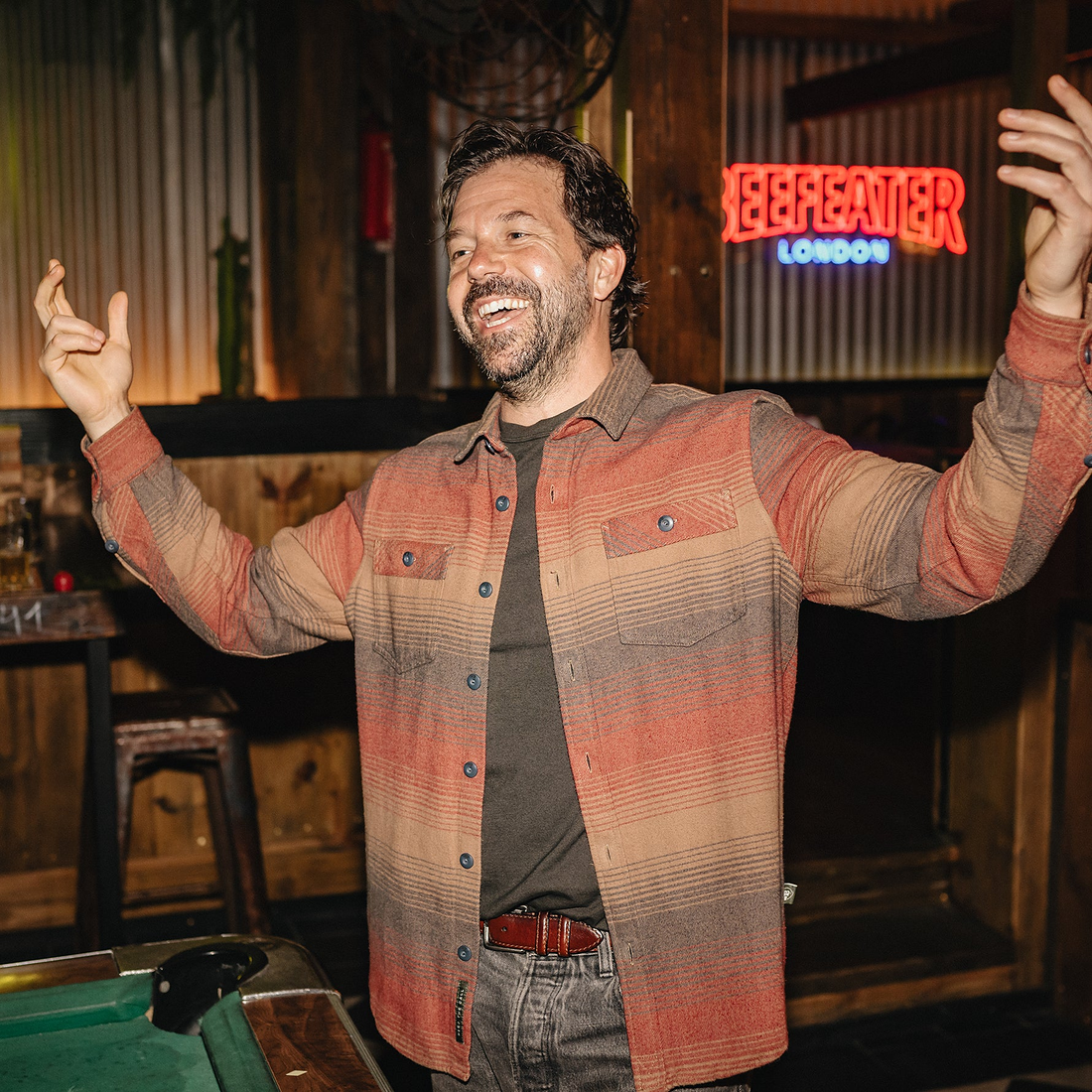 Man in Sunset blanket flannel shirt laughing at a bar