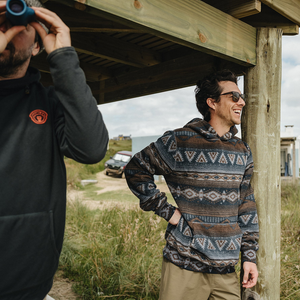 Man in Canyon Codes Tajima hoodie standing under a beach house porch