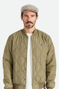 Model wearing Brixton Hooligan Snap Cap in houndstooth with olive quilted bomber jacket