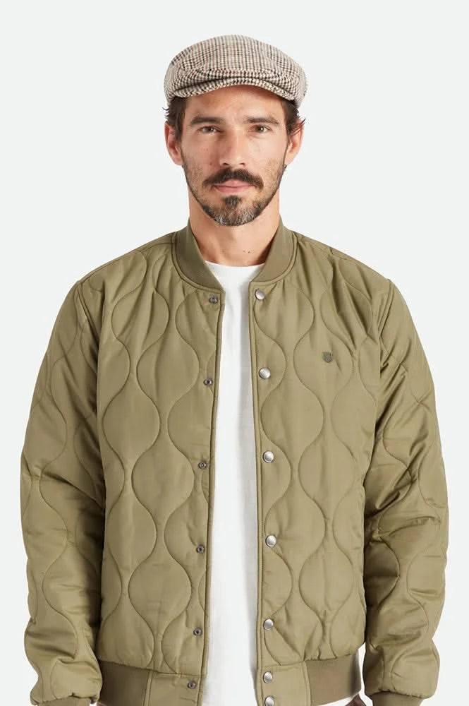Model wearing Brixton Hooligan Snap Cap in houndstooth with olive quilted bomber jacket