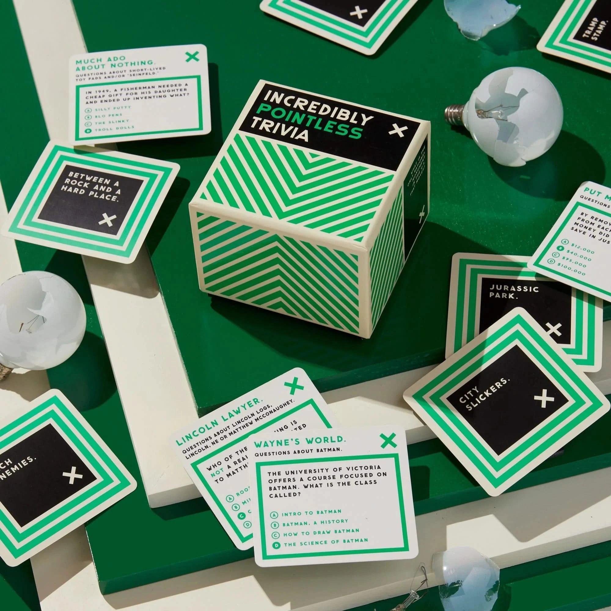 Incredibly Pointless Trivia game by Brass Monkey shown with sample cards. A hilarious trivia game for men featuring 200 absurd questions in a bold green and black box.