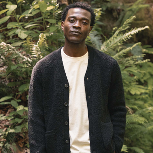 Man wearing the Mateo cardigan in black over a cream tee among ferns, front view - The Simple Man