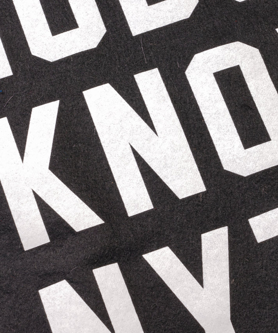 Close-up of Nobody Knows Anything camp flag showing white lettering on black wool felt