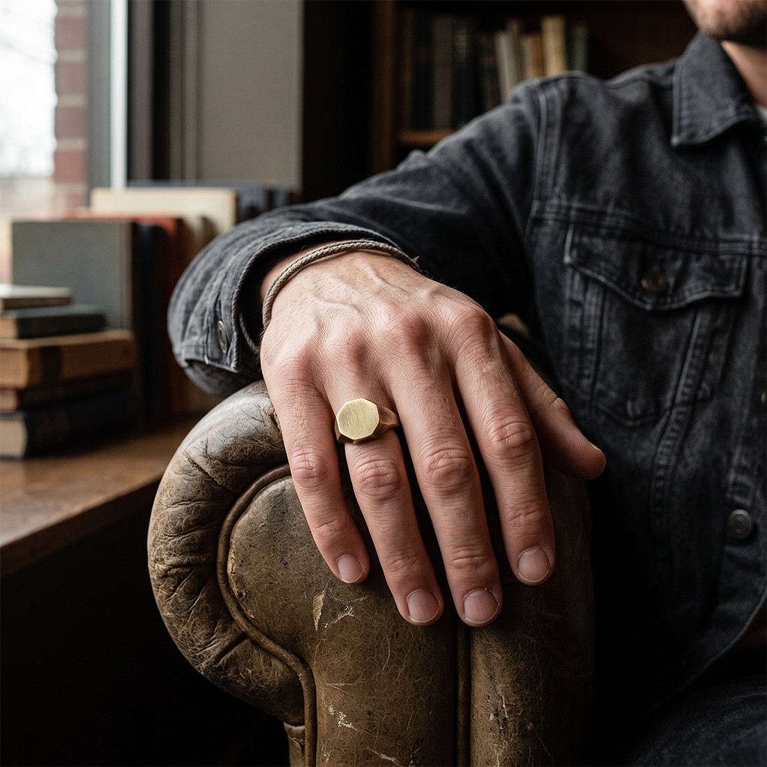 Brass Otto Signet Ring worn on a hand resting on the arm of a worn leather chair