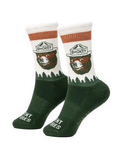 Prevent Wildfires Sock in Spruce lifestyle shot feet up on ottoman by fireplace in cabin with hiking boots showing Smokey Bear knit design