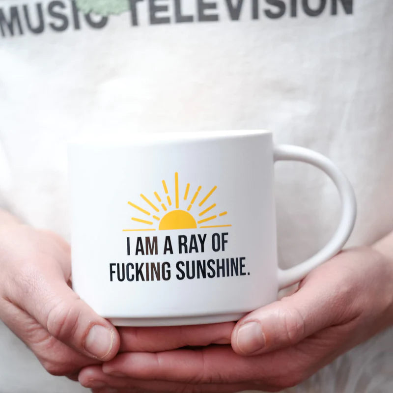 Model Holding Ceramic coffee mug with "I am a ray of fucking sunshine" screened on it with a yellow sun.