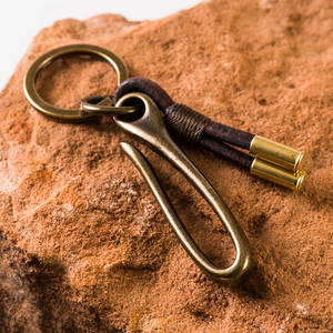 Brass belt hook key chain with a flat ring and two brass .22 shell casings on brown leather, resting on red sandstone