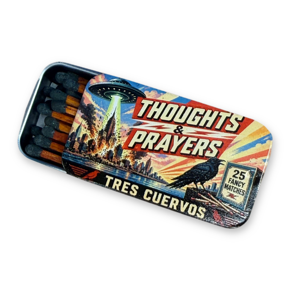 Tin matchbox slid open to show dark-tipped matches, lid showing a UFO over a burning city and the words Thoughts & Prayers
