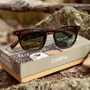 Topo Smokey Bear Edition sunglasses with G15 lenses resting on the Smokey Bear box at a campsite