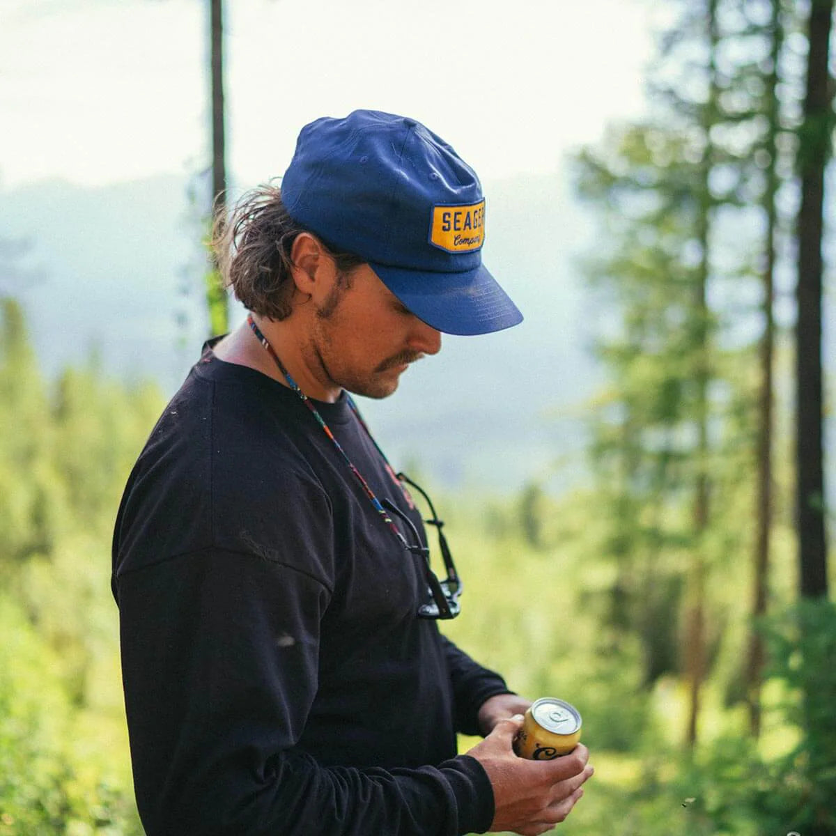 Man wearing navy and yellow Seager Wilson Snapback Hat outdoors in a wooded setting