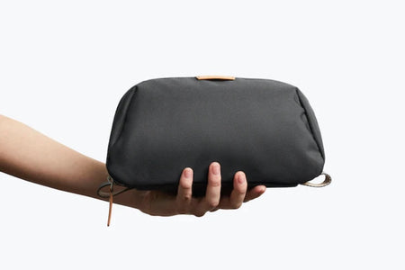 Bellroy Toiletry kit Plus In Charcoal closed in model's hand showing size relationship