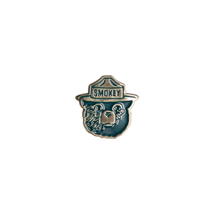 Close-up of the Smokey Bear enamel pin in teal and cream